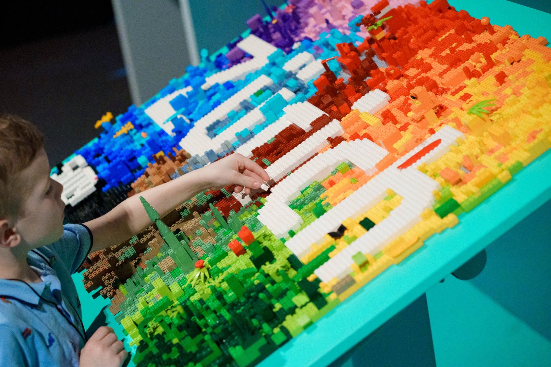 A child pressing bricks into a large multicoloured Lego mosaic on a workshop table